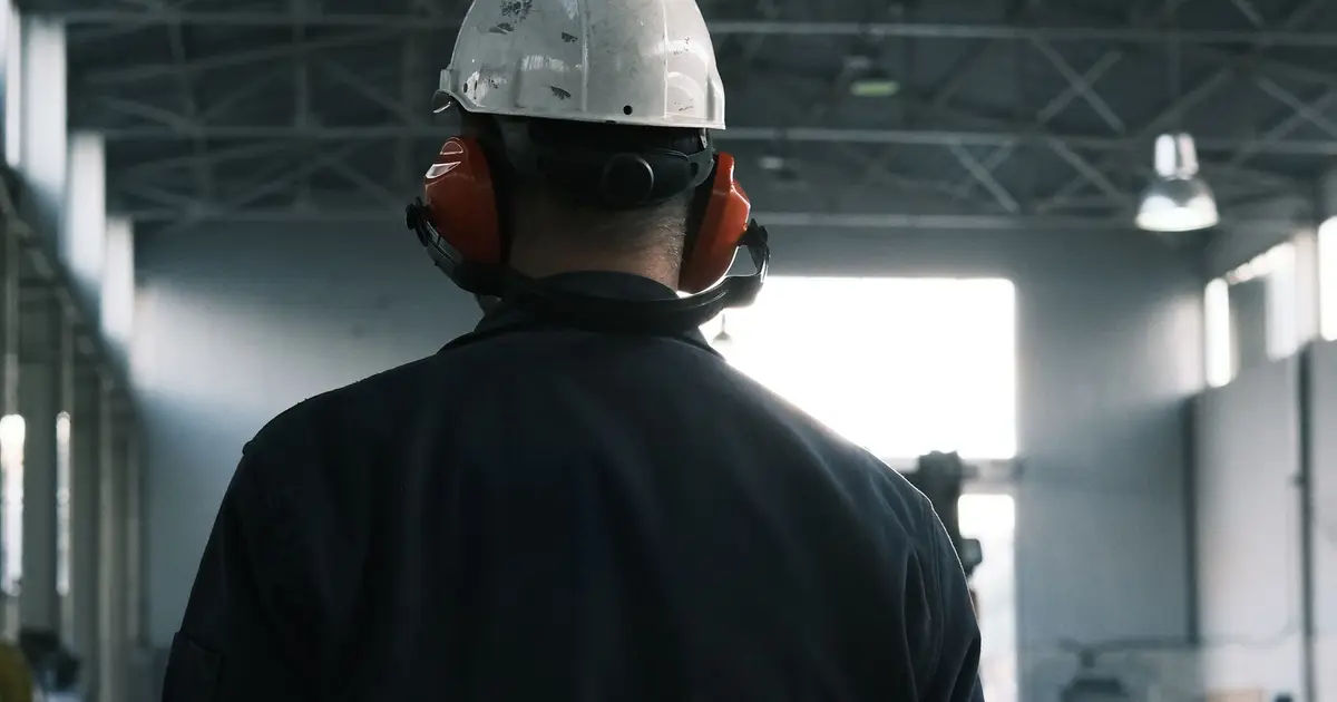 Worker in a hard hat and ear protection walking through a plant bay